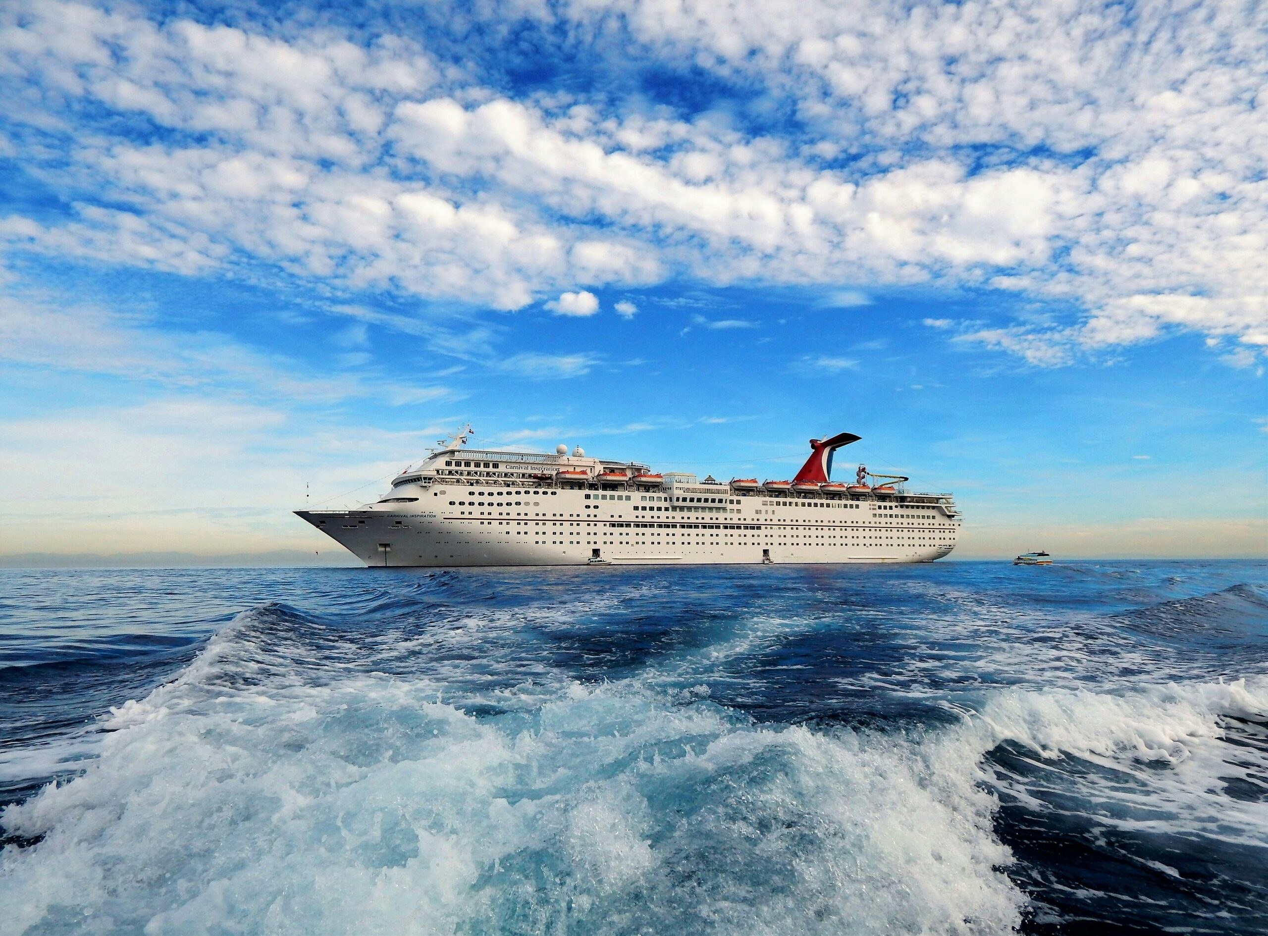 A majestic cruise ship sails on the open sea beneath a vivid blue sky, framed by white clouds.