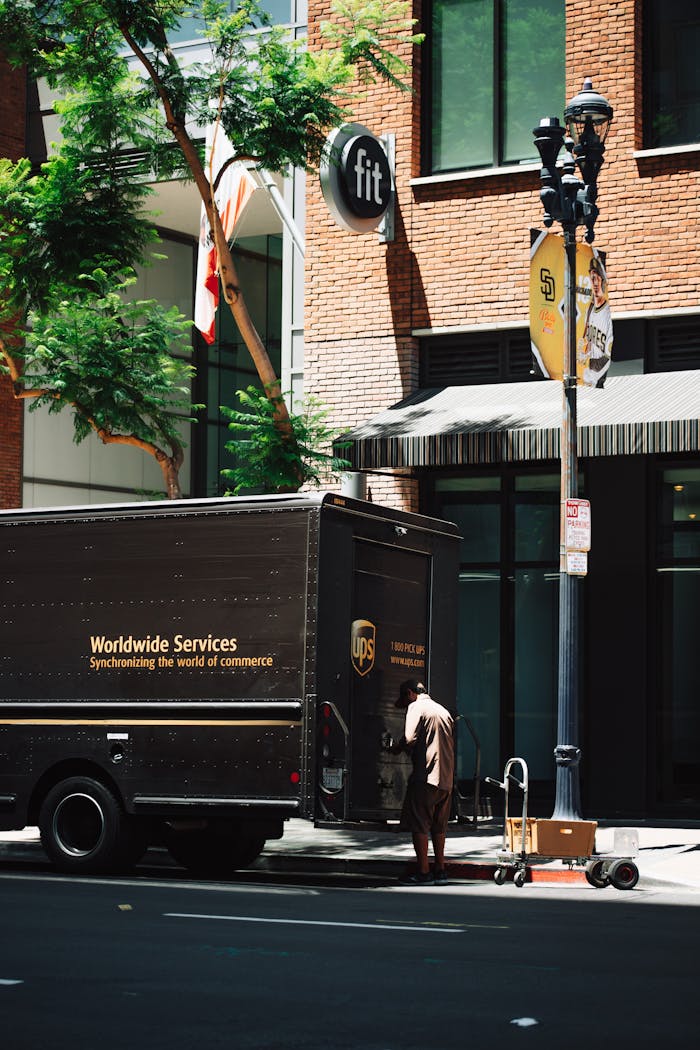 UPS delivery courier loading packages into truck on urban street, showcasing transportation and logistics.