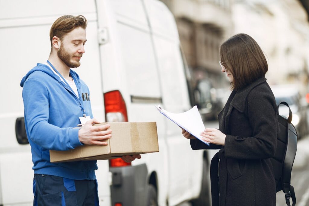 A courier hands over a package to a woman client on a city street, facilitating delivery service.
